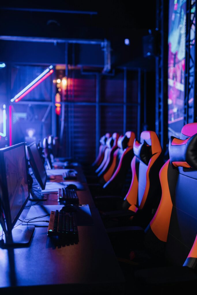 A row of gaming computers and chairs in a dimly lit gaming arena with neon lights.